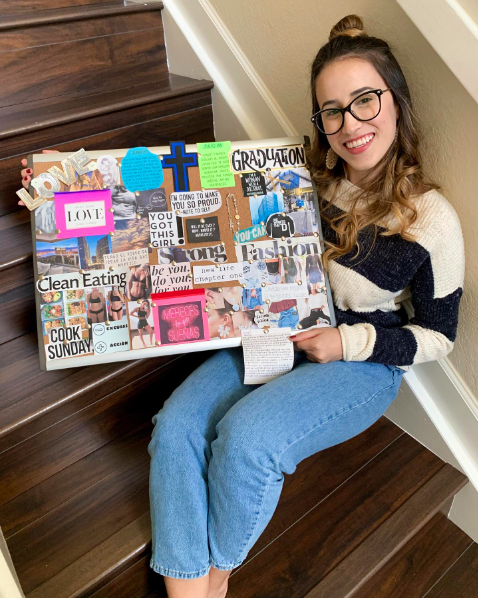 a proud teenage girls sits on a staircase displaying her vision board 