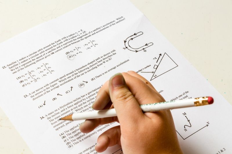 Student holding a pencil and taking a math test on a printed page laying on a desk