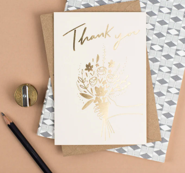 A pretty thank you card laid out on a table with a pencil and pencil sharpener