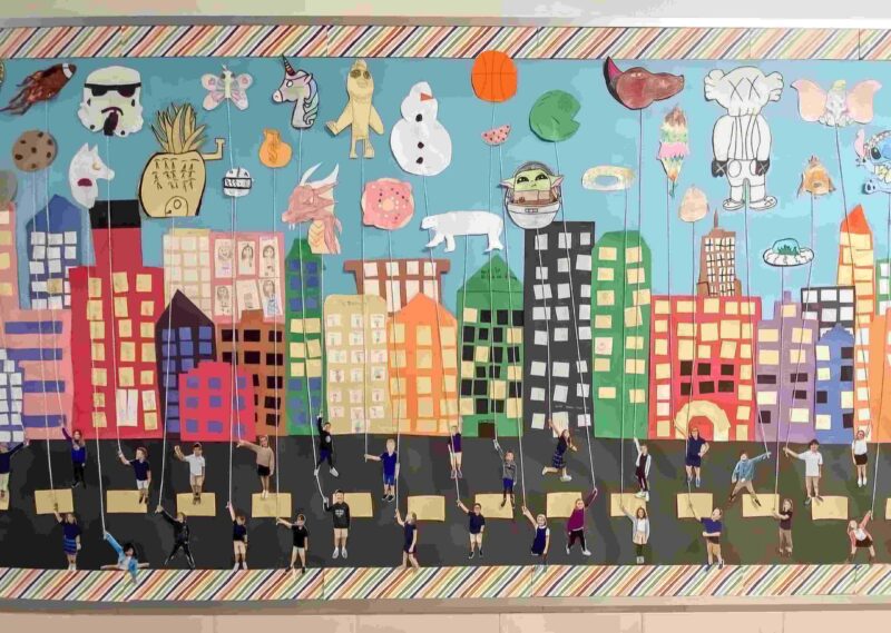 Thanksgiving Bulletin Board: Parade Thanksgiving bulletin board showing photos of students holding parade balloons they've created with buildings in the background