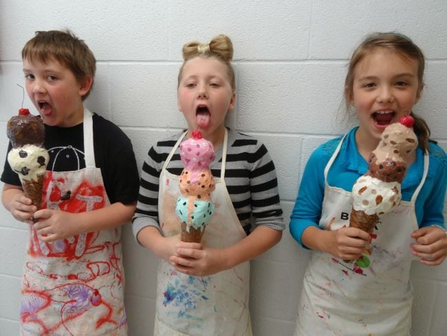 Three third grade art students pretending to eat paper mache ice cream cones