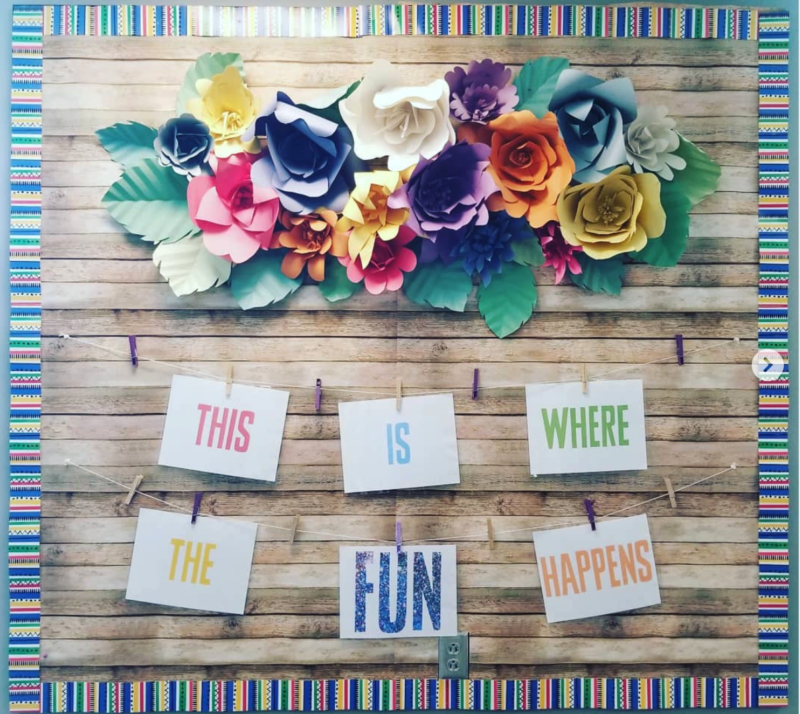Bulletin board with large paper flowers and word signs reading This Is Where The Fun Happens