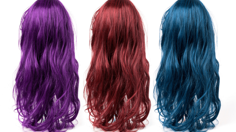 Three brightly colored wigs, one purple, one red, and one blue