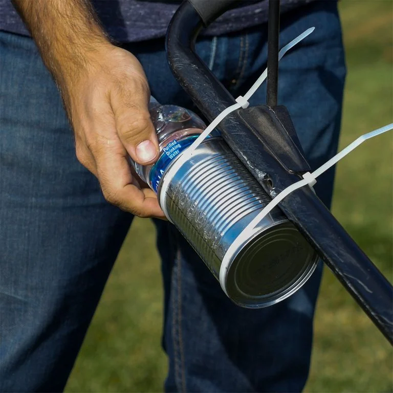 A hand is seen holding a water bottle that is inside a tin can and strapped to a handle by zip ties.