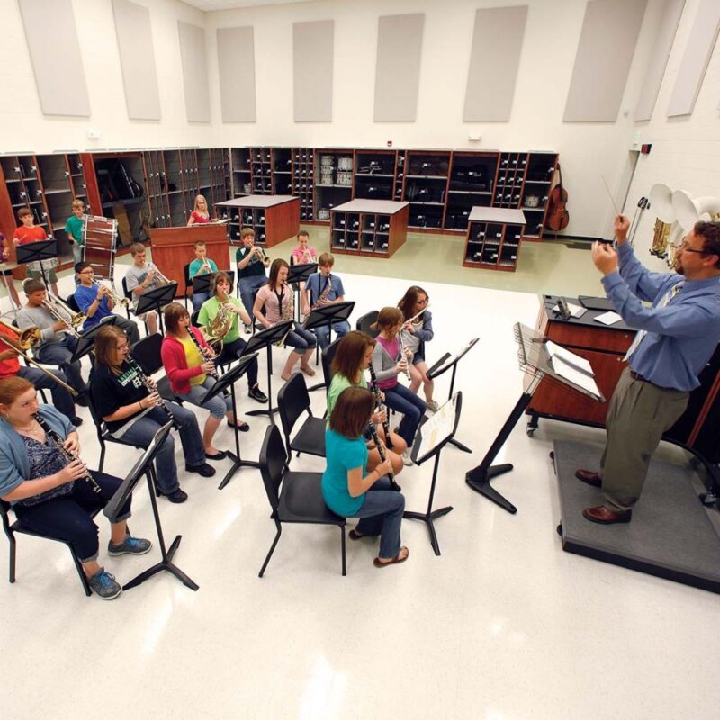 Students sitting in chairs playing musical instruments in a classroom with traditional acoustical panels on the walls