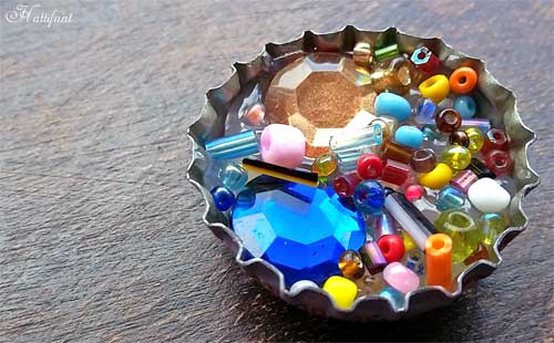 A bottle cap is filled with beads and gems. 
