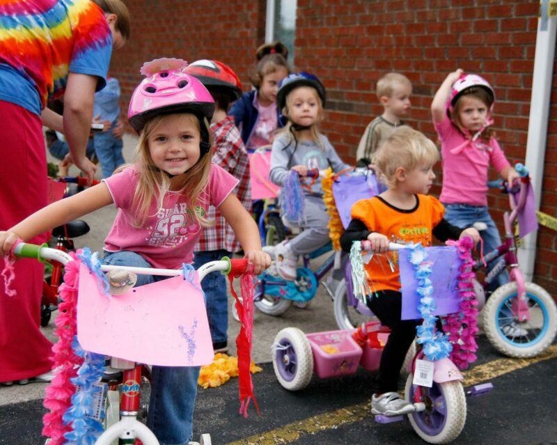 Colorfully dressed preschoolers riding decorated tricycles