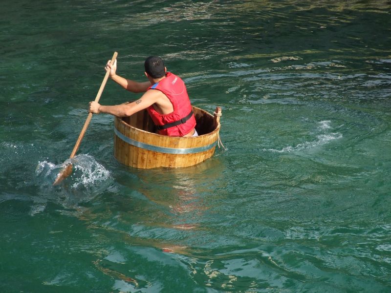 Man wearing a life jacket and paddling half a barrel in a lake