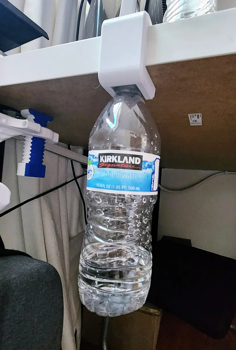 A table has a small white clip attached to it with a water bottle hanging down underneath it.