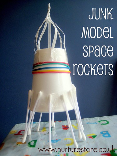 A rocket ship is constructed from a white paper cup, elastics, toothpicks, and other found objects. 