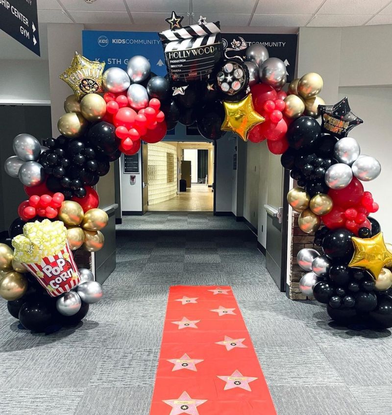 Giant Hollywood-themed balloon arch with a paper "red carpet" covered in gold stars