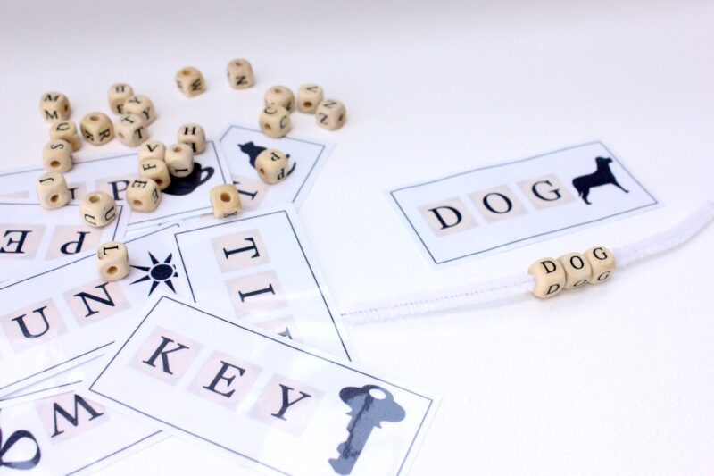 Wooden letter beads threaded onto a pipe cleaner and vocabulary cards with pictures as an example of vocabulary activities