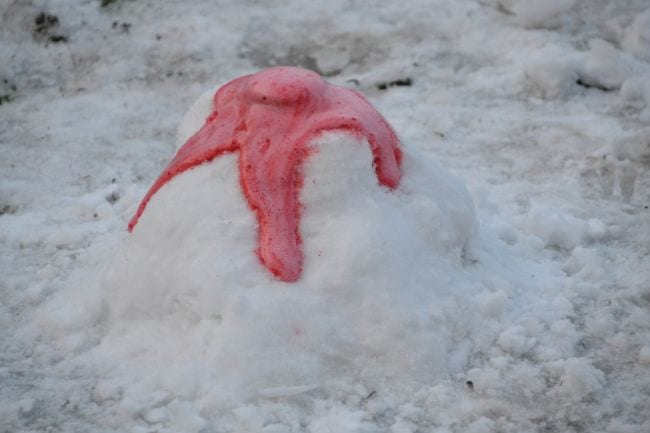Model volcano built from pile of snow with red lava foam erupting from the top