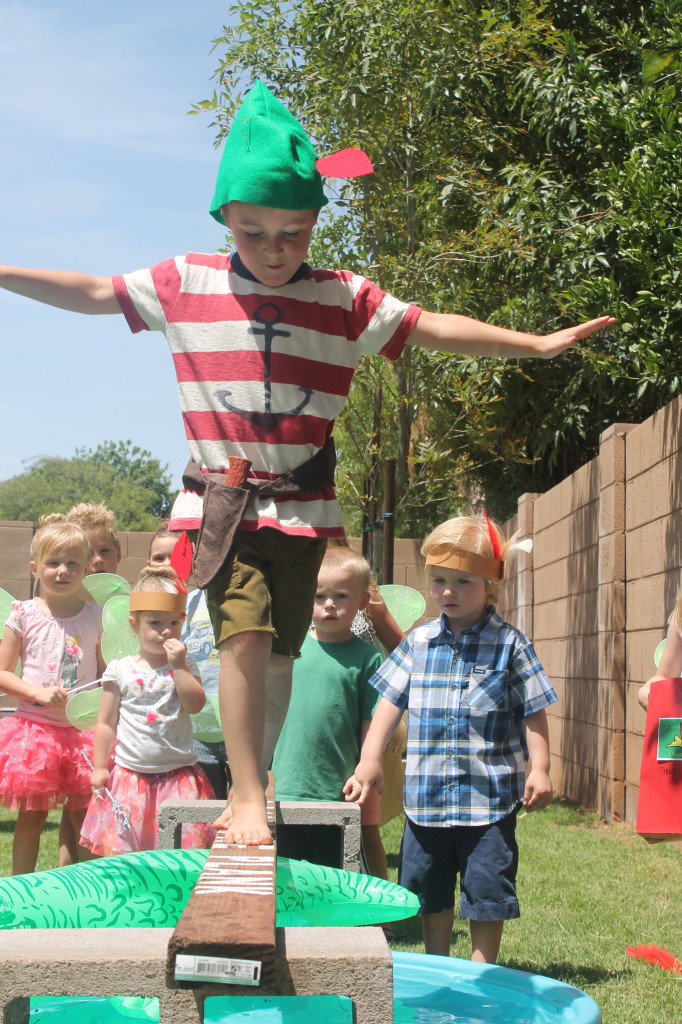 boy walking across a board that is placed over a kiddie pool for a water activity 