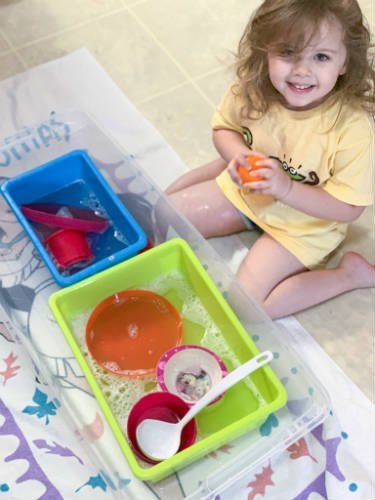 child with two bins filled with water and dishes for water activity washing dishes 