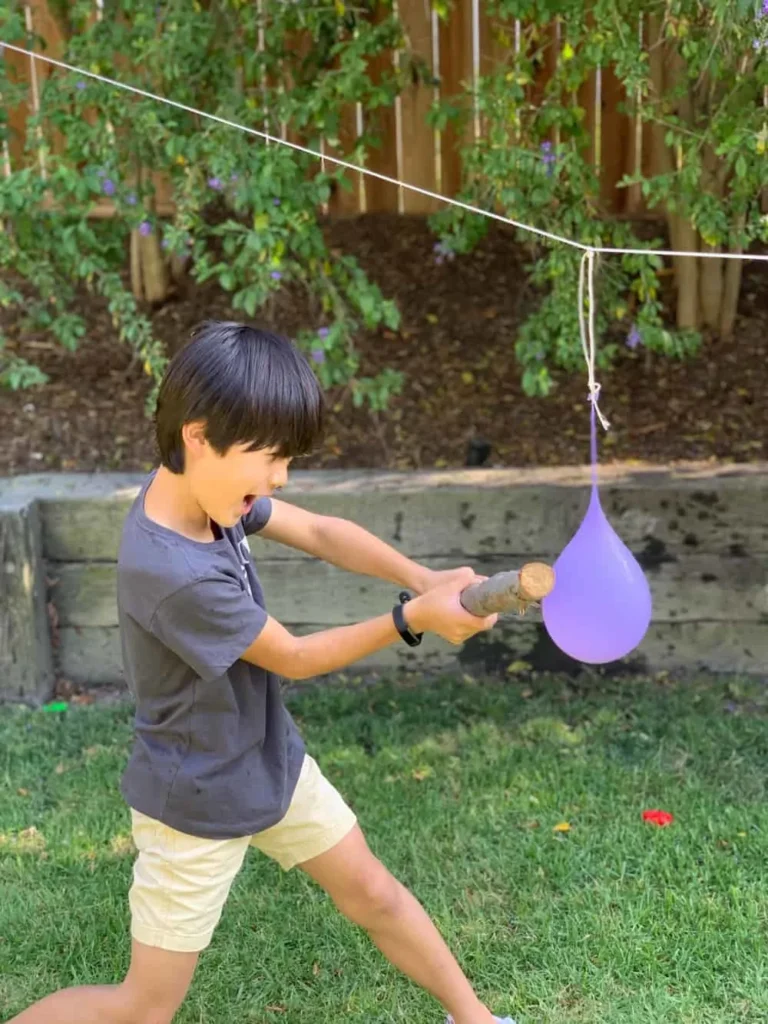 boy swinging at a water balloon hung from a clothesline 
