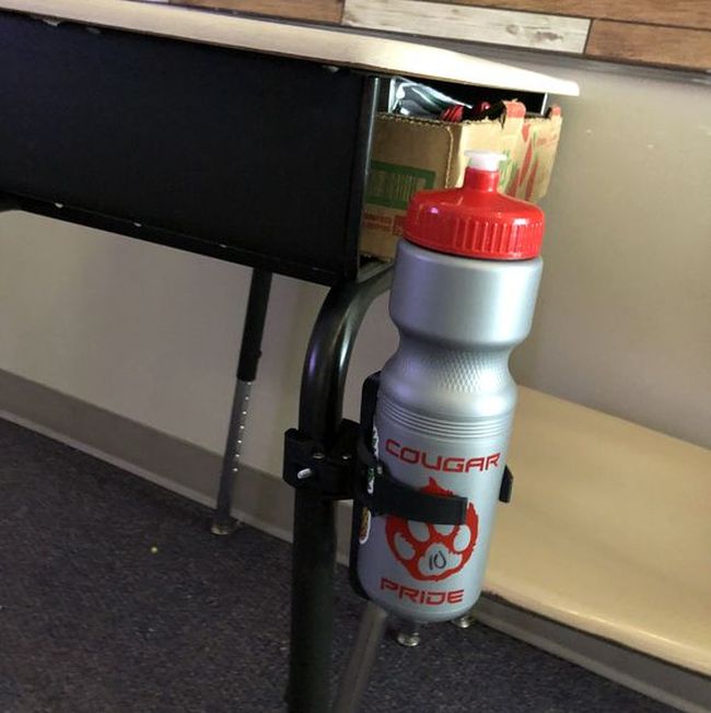 A clamp-on bike water bottle holder attached to a student desk leg