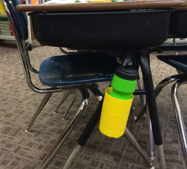 Empty disinfectant wipe bottle wrapped with duct tape and attached to student desk leg to hold a water bottle