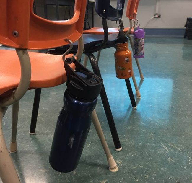 Water bottle holders for student desks include these S hooks attached to student chairs that have a hole drilled in them. water bottles hang off the hooks.