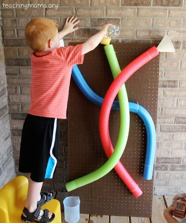 boy standing by a water wall made of pool noodles 