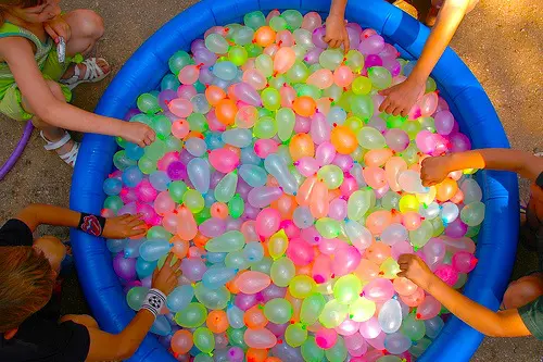 A kiddie pool is filled with neon colored water balloons. 
