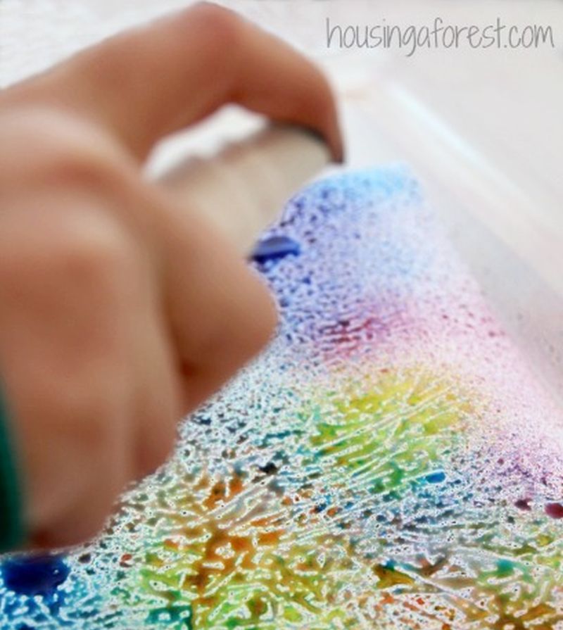 Child spraying colored water onto wax paper 