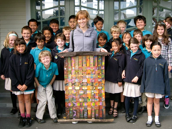 A teacher and students proudly display a colorful woven painting