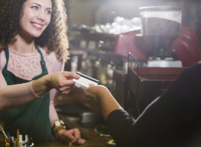 Cropped view of a cashier, a young woman, working in a coffee shop, taking a credit card or gift card from a customer. The main focus is on the hands and the card.