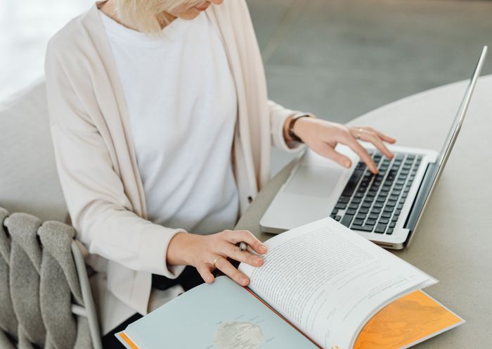 Woman typing on her laptop and holding a book.