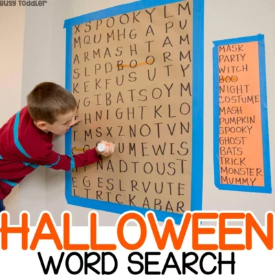 A large word search is taped to the wall and a little boy is searching for words (Halloween activity)