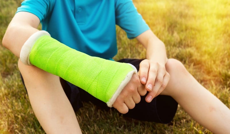 Child with green cast sitting down on grass