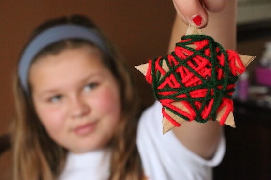 A little girl holds up a green and red yarn wrapped ornament