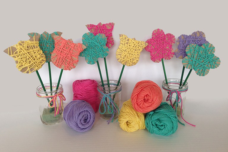 Multiple flowers are made from different shaped pieces of cardboard with different colored yarn wrapped around them (mother's day crafts for kids)