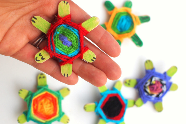 Several turtles are made from popsicle sticks with brightly colored yarn wrapped around them. Faces are drawn on them with sharpie.